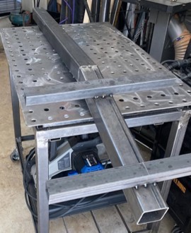 Welded steel base cross-frame clamped on a welding fixture table