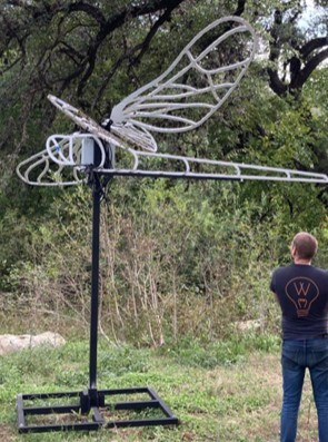 Bare unlit welded-metal dragonfly frame on a mobile stand outdoors during setup