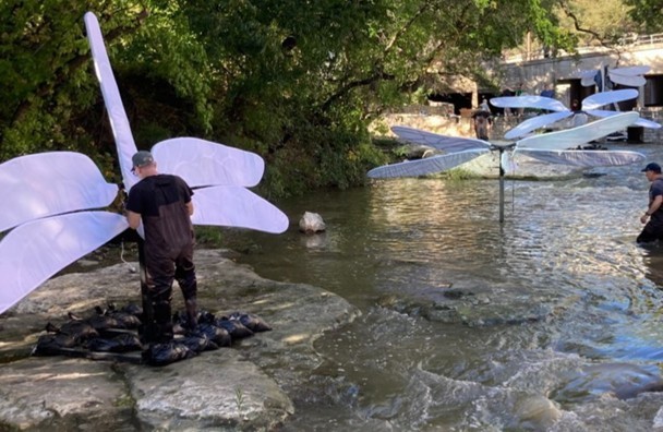 Installer in waders setting a dragonfly sculpture into the creek