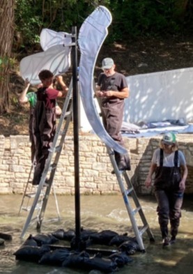 Crew on ladders assembling a large dragonfly wing over the creek