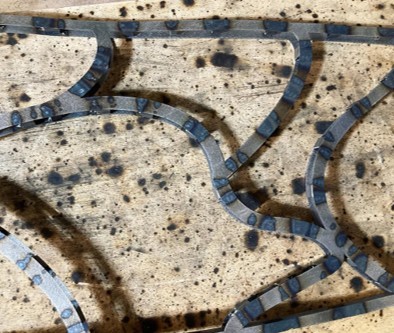 Close-up of a welded, unfinished dragonfly wing frame resting on a scorched wooden jig