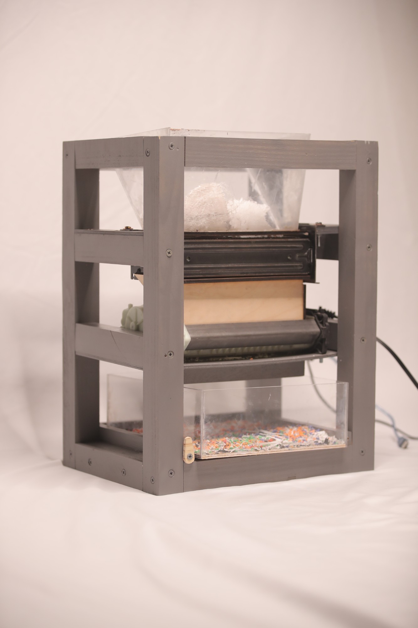 Built ECOFIL shredder in a gray frame: clear hopper on top, cutter in the middle, and a clear bin of shredded multi-color flake below