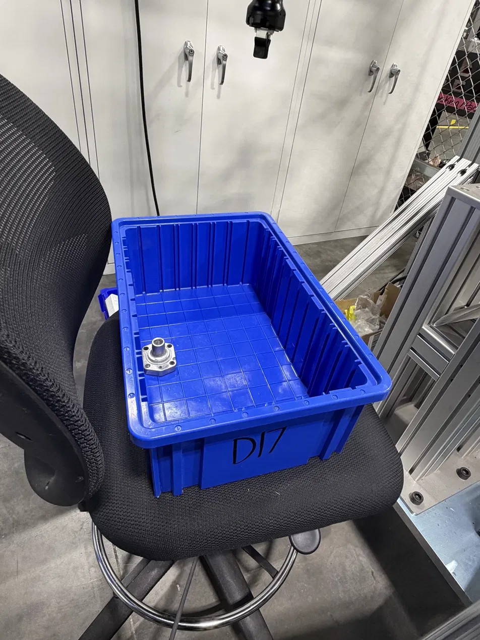 Blue plastic tote holding a single machined flanged component