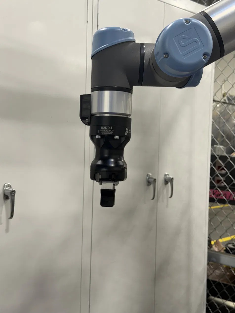 Universal Robots cobot wrist fitted with a Robotiq Hand-E parallel gripper and custom jaws